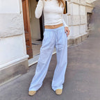 Femme en pull blanc et pantalon ample bleu clair, debout devant un bâtiment en pierre. Mode décontractée, style urbain, tenue confortable.