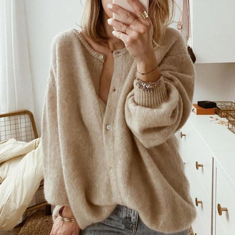 Femme portant un cardigan en laine beige, manches longues, boutons, style décontracté, mode automne-hiver, intérieur moderne, accessoires élégants.