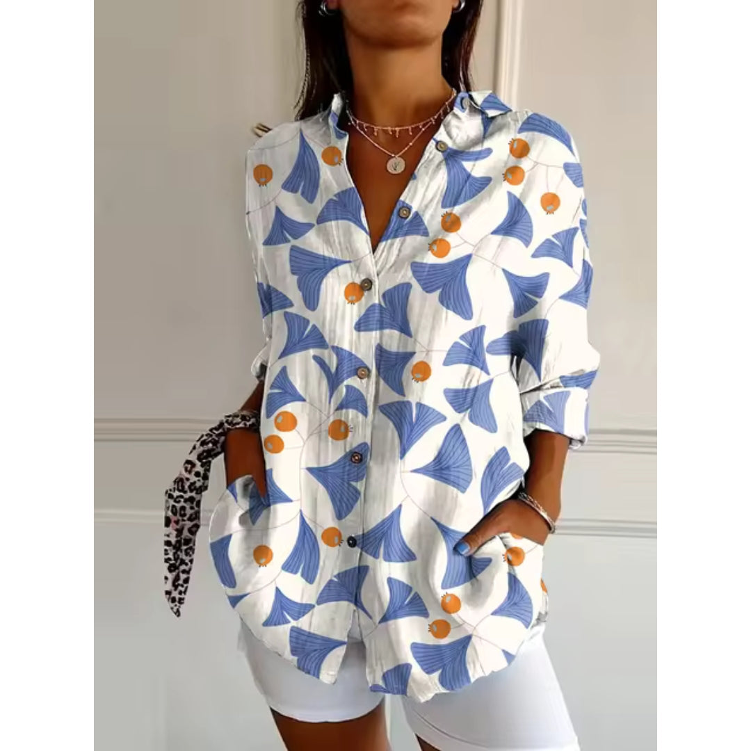 Chemise femme à motifs floraux bleus et oranges, manches longues, col classique, boutons en bois, portée avec short blanc. Mode tendance décontractée.