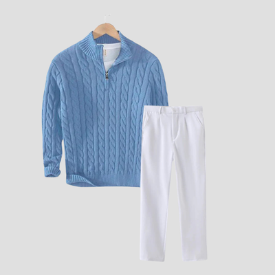 Pull bleu en maille torsadée avec fermeture éclair et pantalon blanc élégant sur fond gris. Mode automne-hiver, tenue décontractée chic.