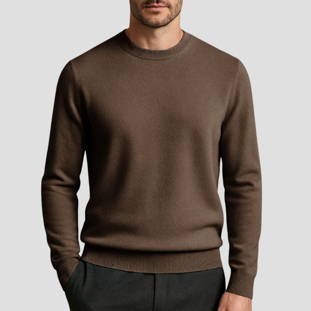 Homme portant un pull marron en laine, col rond, manches longues, sur fond gris. Mode masculine élégante, tenue automne-hiver, style décontracté.