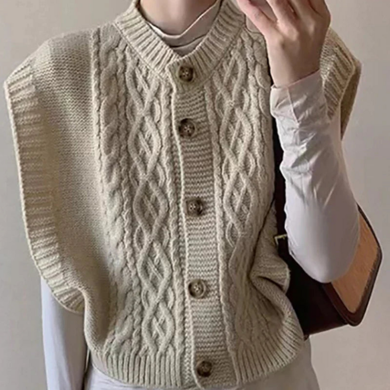 Gilet sans manches en tricot torsadé beige, boutons en bois, porté sur un haut blanc. Mode automne-hiver, style décontracté et élégant.