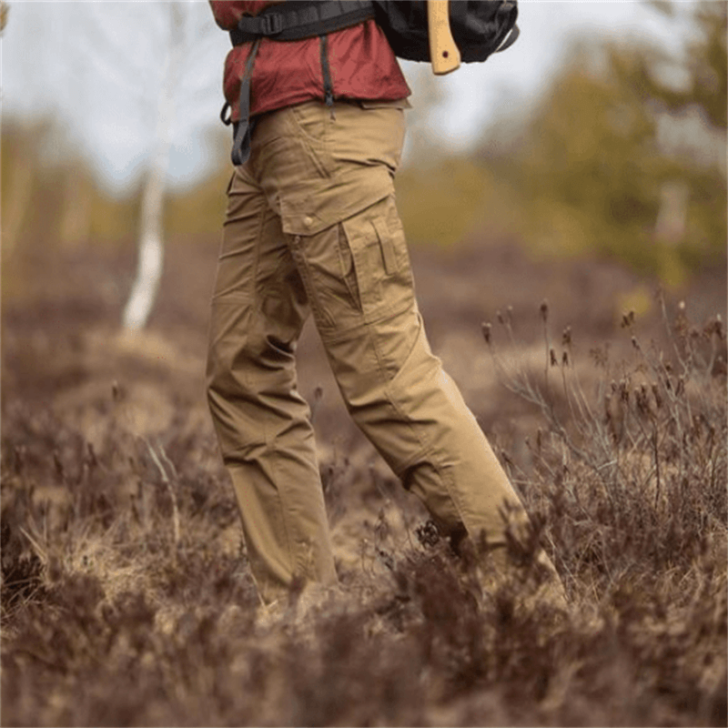 Pantalon cargo marron pour randonnée en plein air, homme avec sac à dos, nature automnale, vêtements résistants, aventure en forêt.