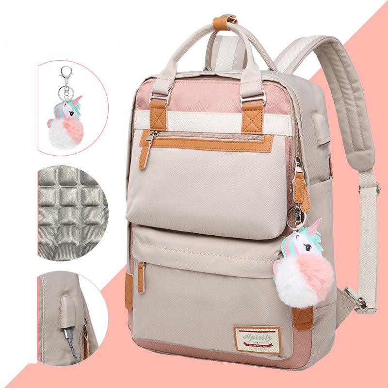 Sac à dos beige et rose avec porte-clés licorne, poches multiples, fermeture éclair robuste et bretelles ajustables. Design moderne et fonctionnel.