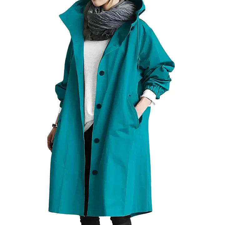 Manteau imperméable turquoise pour femme avec capuche, porté avec écharpe grise et chemise blanche. Mode automne, style décontracté.