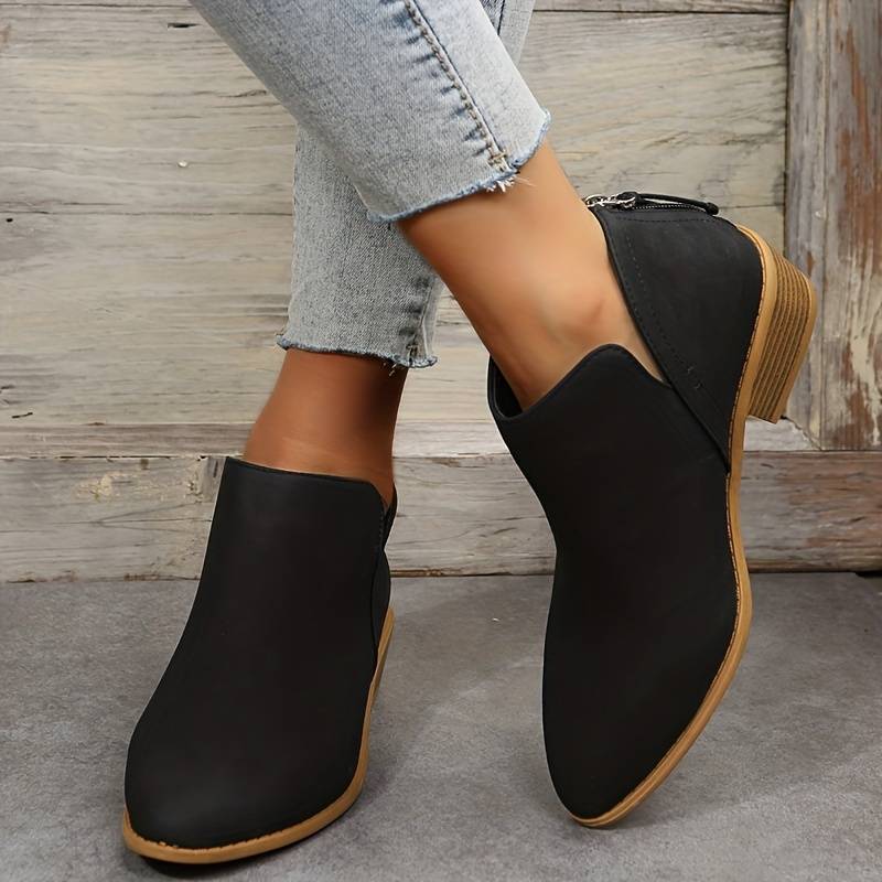 Bottines noires élégantes pour femme avec talons bas, portées avec un jean décontracté. Chaussures tendance automne, style moderne et confortable.