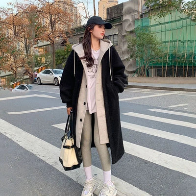 Femme en manteau long noir et gris, leggings gris, baskets blanches, casquette noire, sac à main, traverse une rue urbaine. Mode automne-hiver tendance.