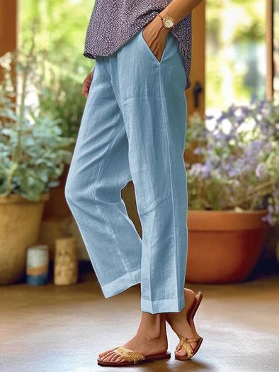 Pantalon en lin bleu clair pour femme, coupe décontractée, poches latérales, porté avec des sandales dorées, ambiance estivale et décontractée.