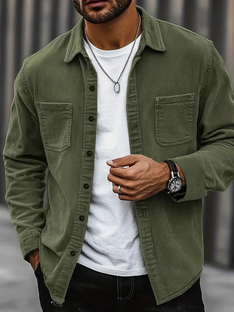 Homme portant une chemise en velours côtelé vert, t-shirt blanc, montre noire et collier argenté. Mode masculine décontractée et élégante.