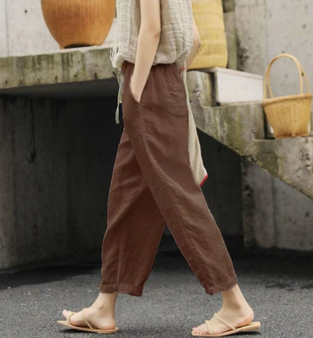 Personne portant un pantalon marron ample et des sandales, marchant sur un trottoir. Panier en osier et mur en béton en arrière-plan. Mode décontractée.