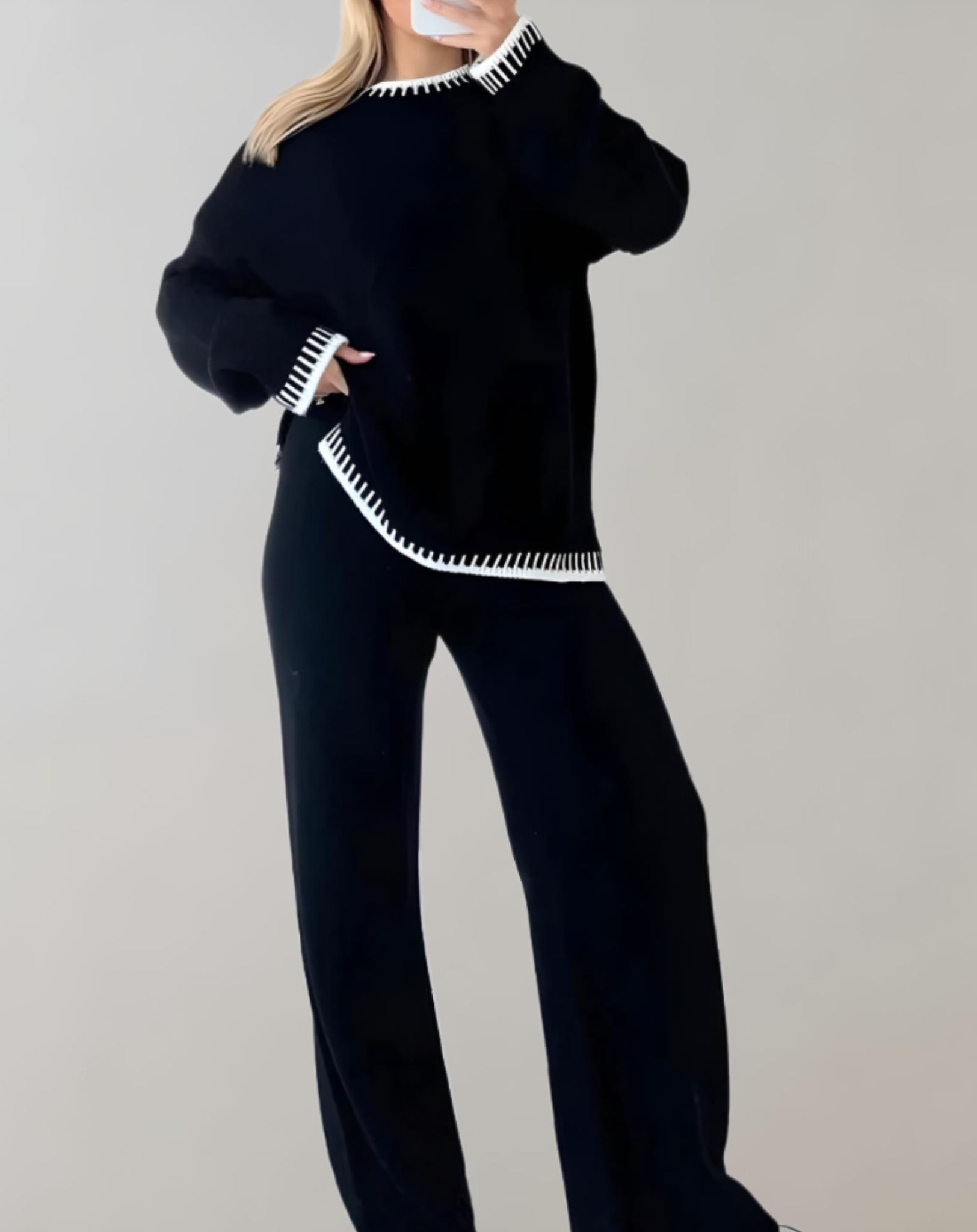 Femme portant un ensemble noir élégant avec bordures blanches, composé d'un pull ample et d'un pantalon large. Mode automne-hiver chic et confortable.