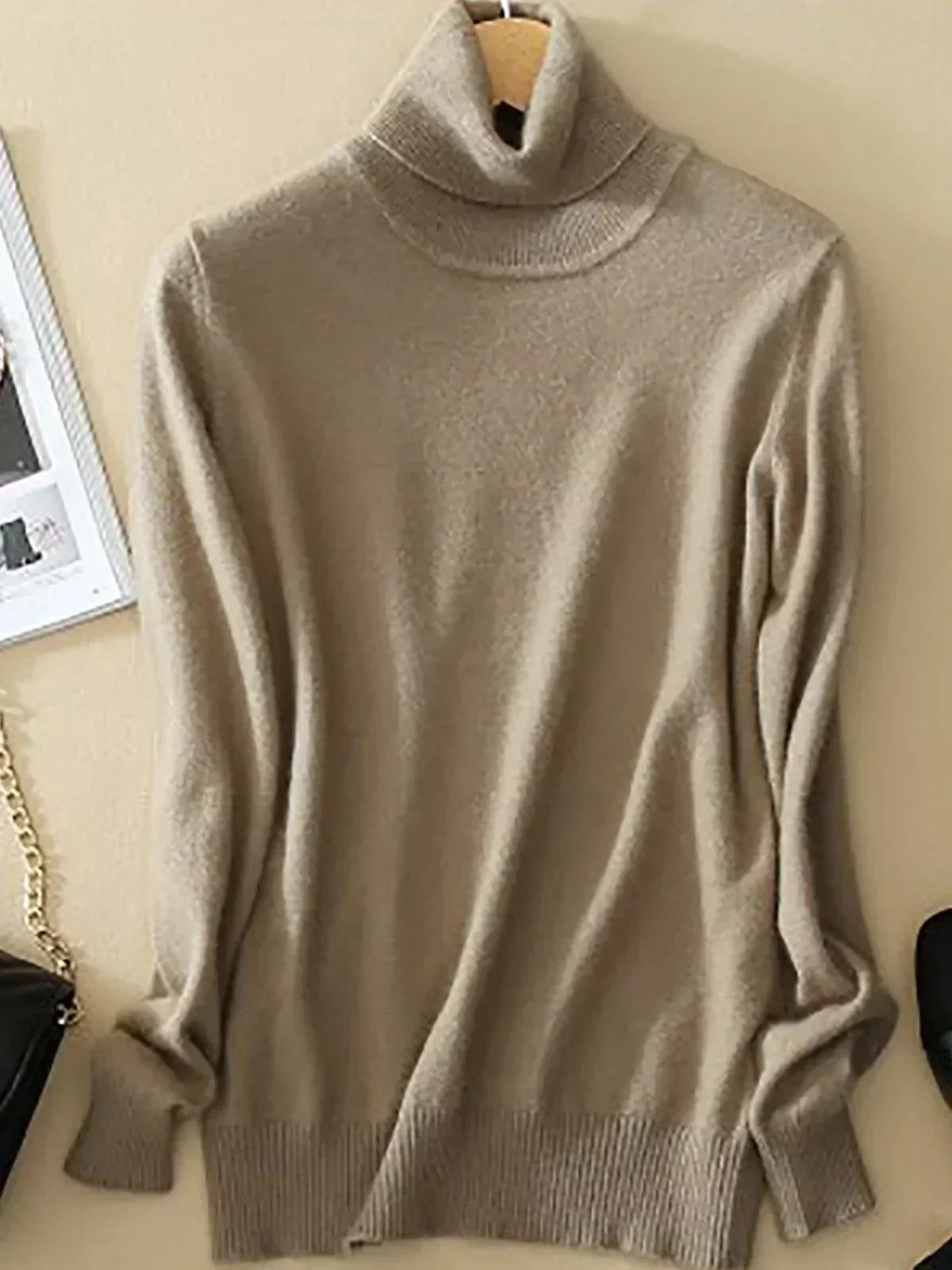 Pull col roulé beige en laine, suspendu sur un cintre, avec texture douce et manches longues. Mode automne-hiver, vêtement chaud et élégant.