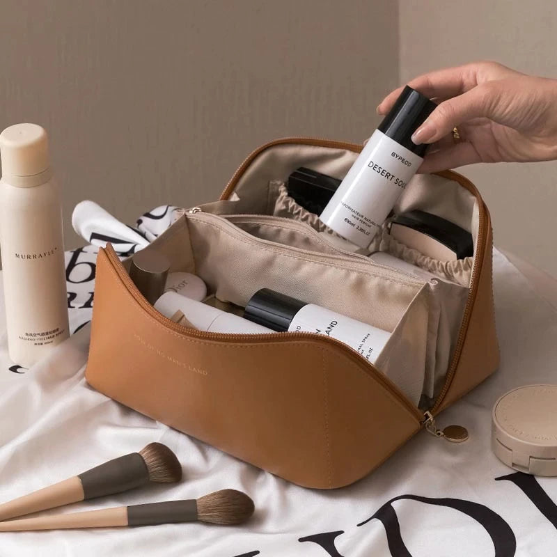 Trousse de maquillage en cuir marron avec produits de beauté et pinceaux, main tenant un flacon. Accessoires cosmétiques élégants sur tissu blanc.