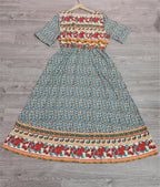 Robe longue bohème à motifs floraux colorés, manches courtes, fond bleu, accrochée sur un cintre en bois, posée sur un sol en bois gris.