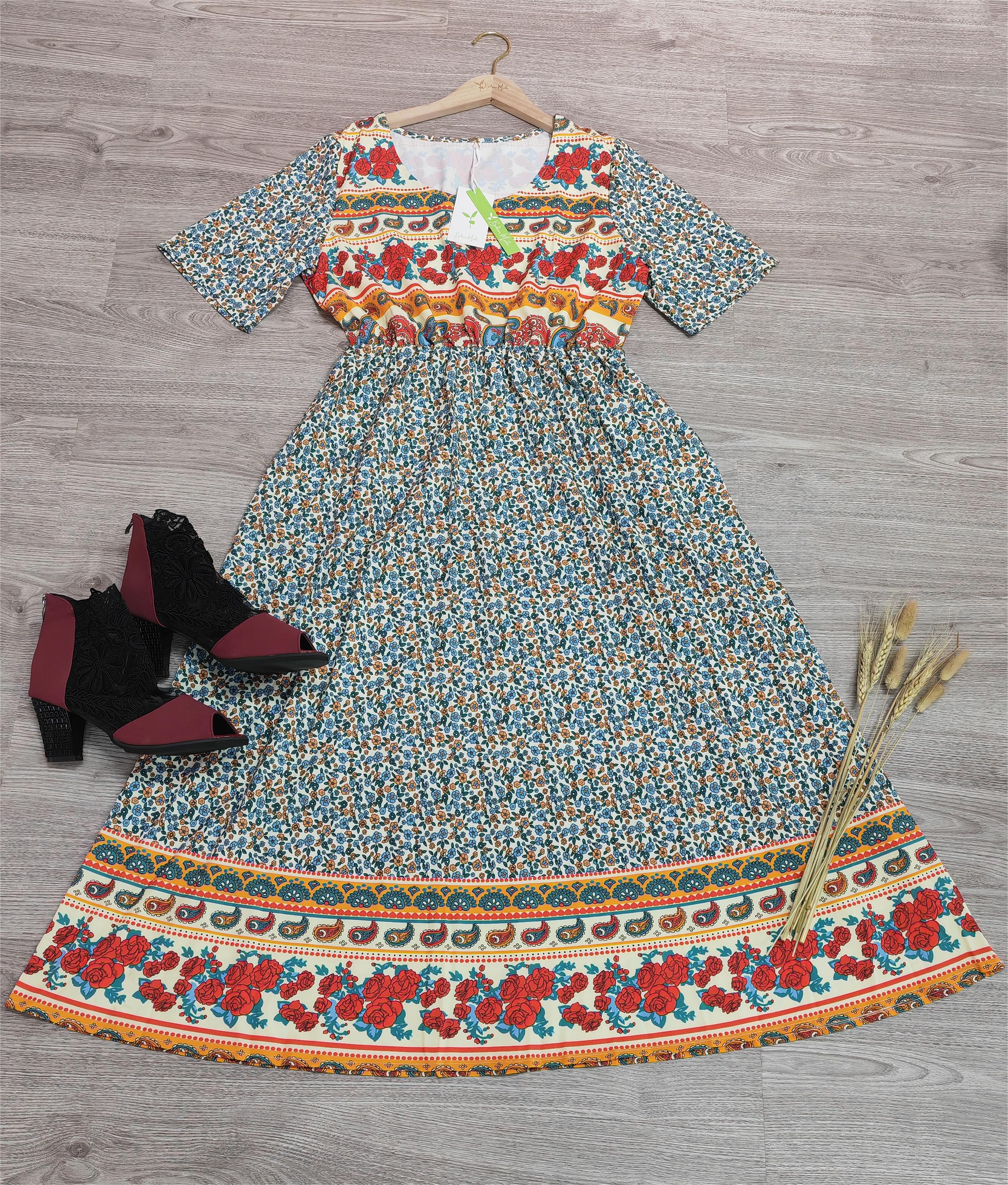 Robe longue bohème à motifs floraux colorés sur fond gris, manches courtes, accompagnée de bottines noires et épis de blé décoratifs.