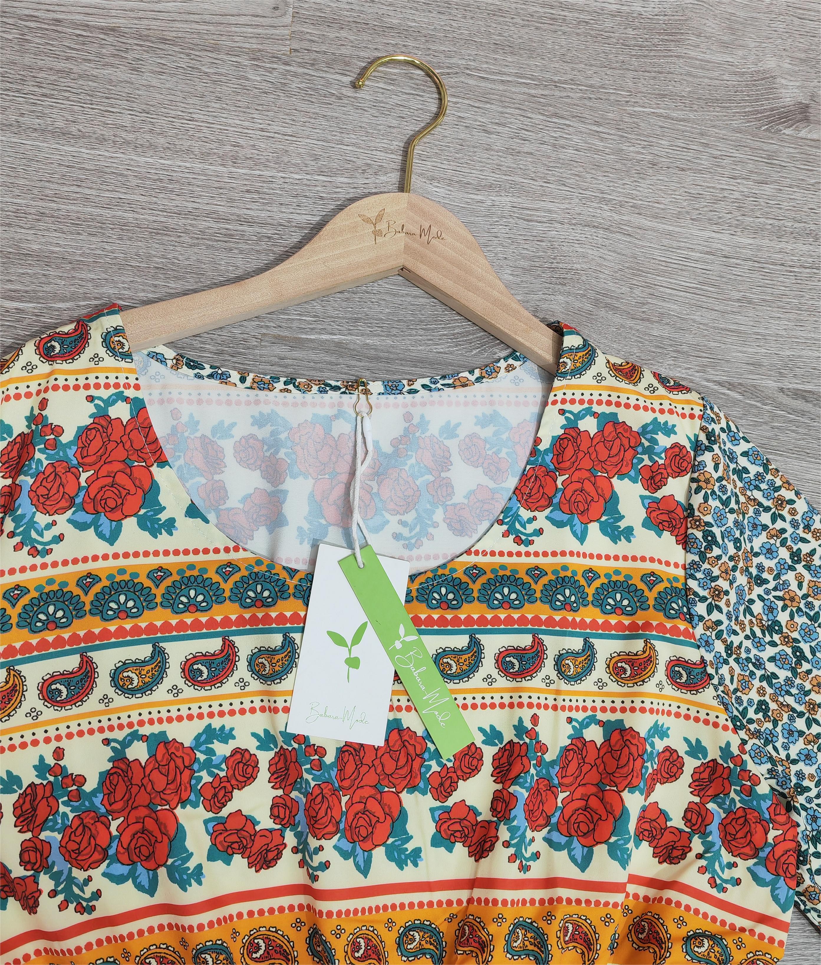 Robe bohème à motifs floraux rouges et bleus sur cintre en bois, fond en bois clair. Mode féminine, style vintage, tendance été.