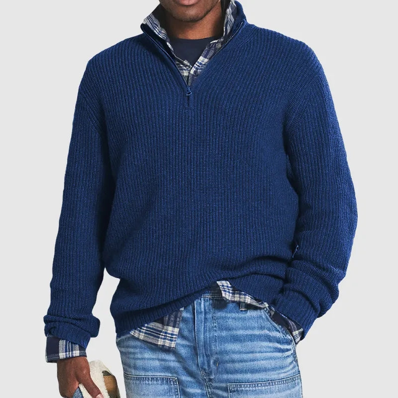 Homme portant un pull bleu à col zippé sur une chemise à carreaux, avec un jean décontracté. Mode masculine, tenue automne-hiver élégante.