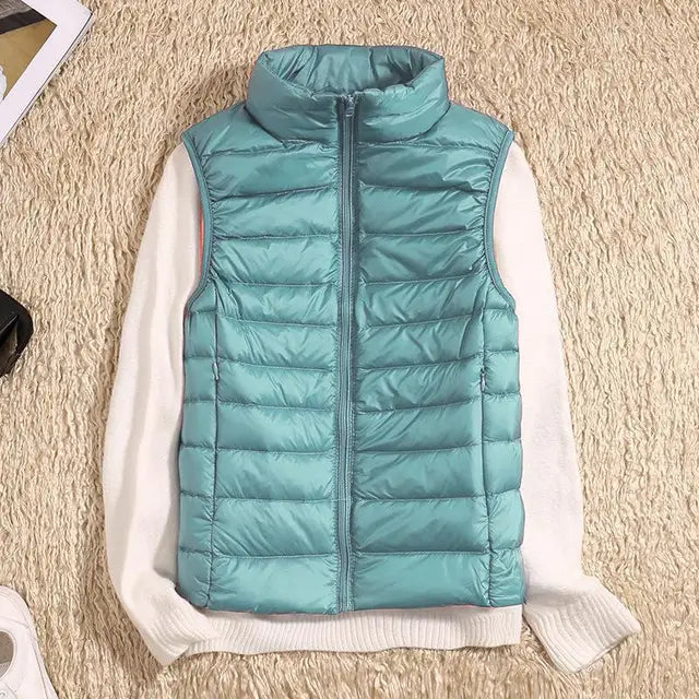 Gilet sans manches matelassé bleu clair sur pull blanc, posé sur tapis beige. Mode automne-hiver, vêtement chaud et tendance pour femme.