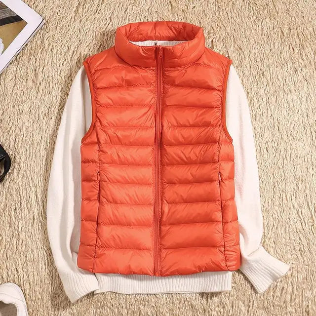 Gilet sans manches orange en duvet sur pull blanc, posé sur tapis beige. Mode automne-hiver, vêtements chauds, style décontracté.