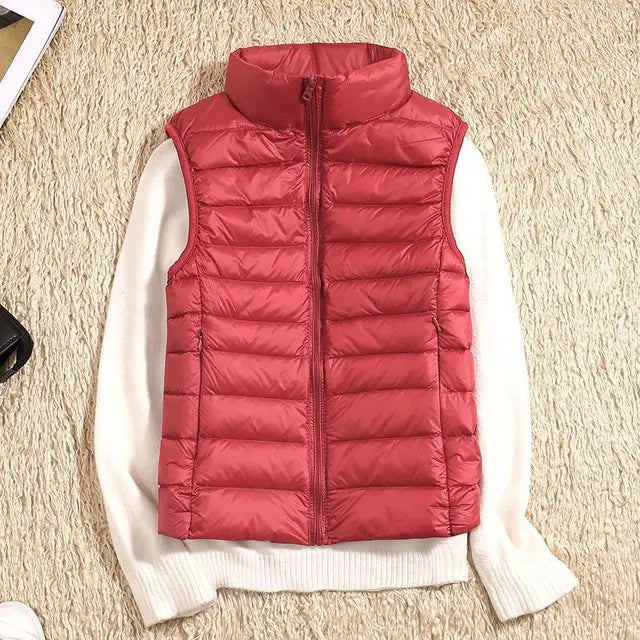 Gilet sans manches rouge matelassé sur pull blanc, posé sur tapis beige. Mode hiver, vêtements chauds, style décontracté.