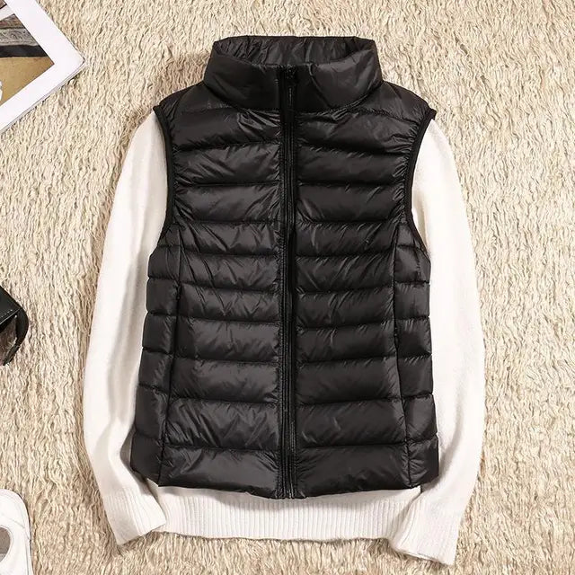 Gilet sans manches noir en duvet sur pull blanc, posé sur tapis beige. Mode hiver, vêtements chauds, style décontracté, tendance automne-hiver.