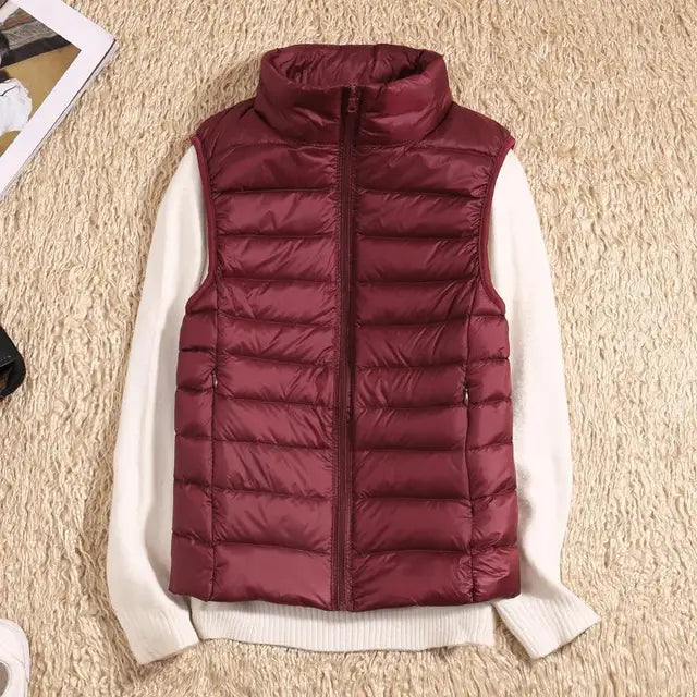 Gilet matelassé bordeaux sans manches sur pull blanc, posé sur tapis beige. Mode automne-hiver, vêtements chauds, style décontracté.