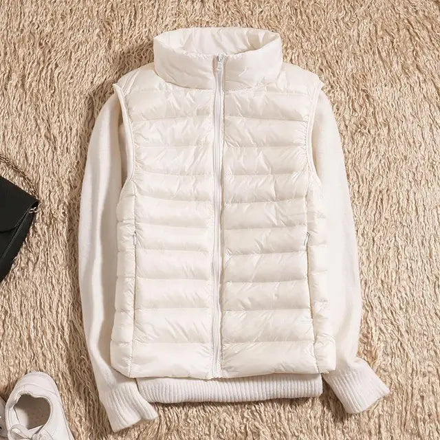 Gilet matelassé blanc sans manches sur un pull blanc, posé sur un tapis beige. Mode hiver, vêtements chauds, style décontracté.