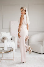 Femme blonde élégante en combinaison rose pâle, posant dans un salon moderne. Mode féminine, style chic, décoration intérieure contemporaine.