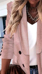 Femme en blazer à chevrons rose, chemise blanche, collier chaîne, cheveux blonds ondulés. Mode élégante, tenue chic, style décontracté.