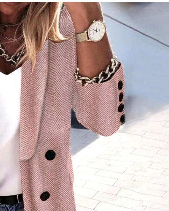 Blazer à motif chevrons rose, boutons noirs, porté par une femme avec montre dorée et collier chaîne, style chic et tendance.