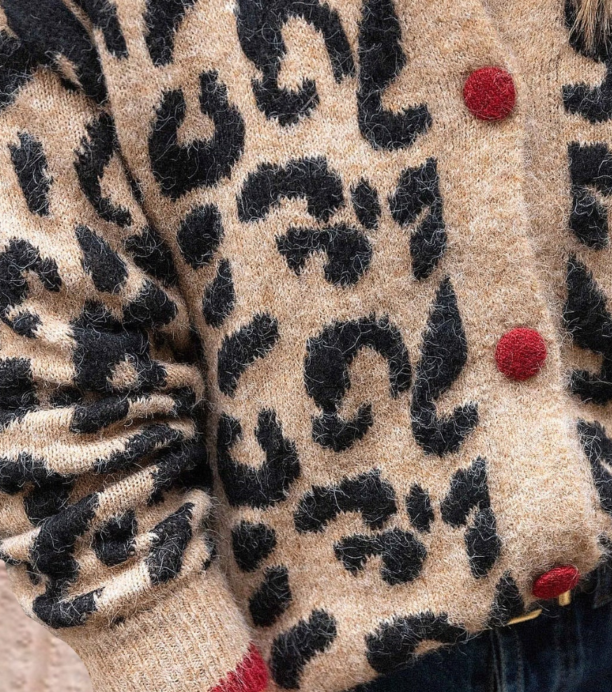 Cardigan en laine à motif léopard noir sur fond beige, boutons rouges distinctifs, manches longues, style tendance et confortable pour l'hiver.