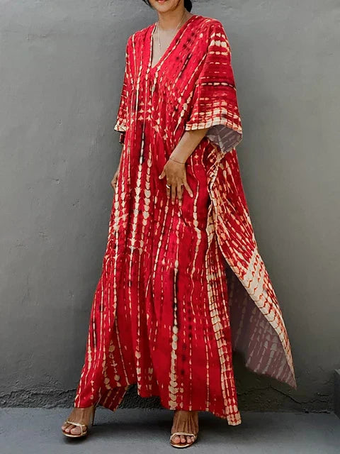 Robe longue rouge à motifs tie-dye, manches larges, portée par une femme debout contre un mur gris. Mode bohème chic, style décontracté.