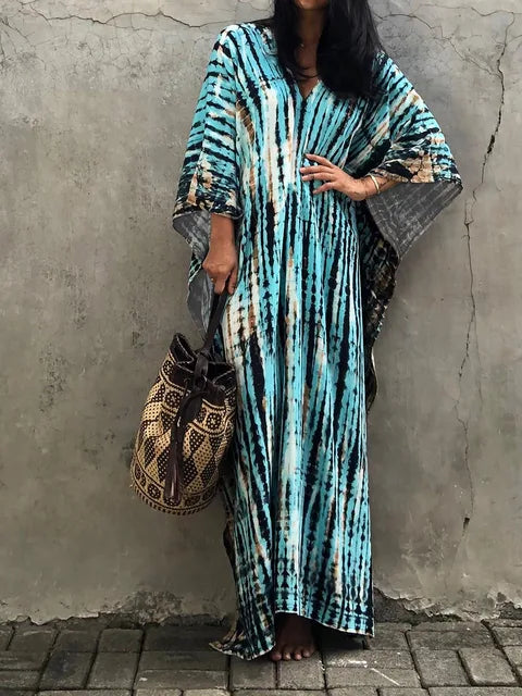 Robe longue bohème bleue et noire à motifs tie-dye, portée par une femme tenant un sac en osier. Mode estivale chic et décontractée.