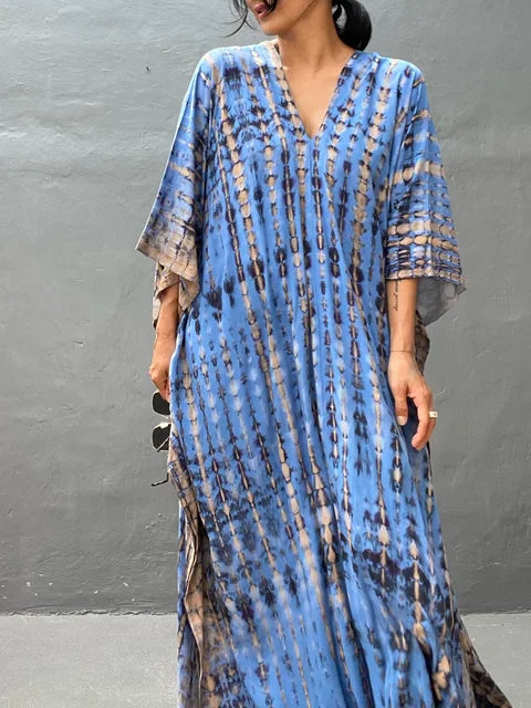 Robe longue bleue à motifs tie-dye, manches larges, portée par une femme. Mode bohème chic, tendance été, style décontracté élégant.
