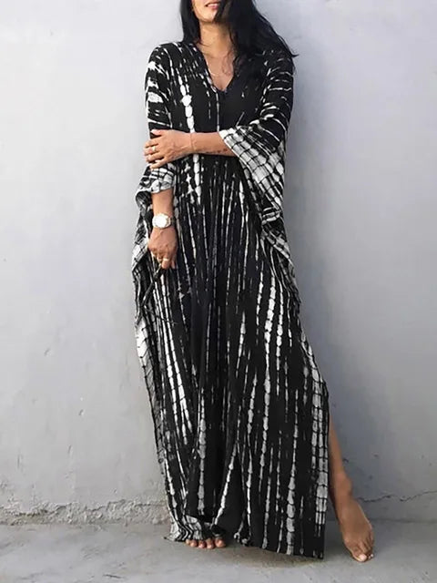 Robe longue noire et blanche à motifs tie-dye, manches longues, portée par une femme contre un mur gris. Mode bohème chic, tendance et élégante.
