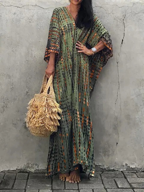 Robe longue bohème verte à motifs ethniques, femme tenant un sac en paille tressée, mode estivale décontractée, mur en arrière-plan.