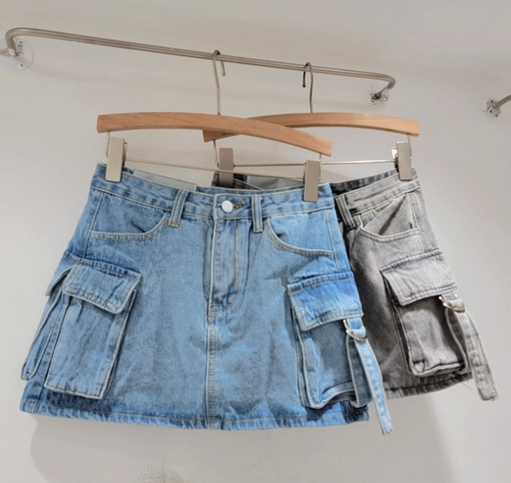 Deux jupes en jean, l'une bleue et l'autre grise, avec poches cargo, suspendues sur des cintres en bois. Mode tendance, vêtements décontractés.