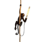Singe en résine grimpant une corde, tenant une ampoule LED allumée. Lampe design originale, éclairage intérieur, décoration moderne.