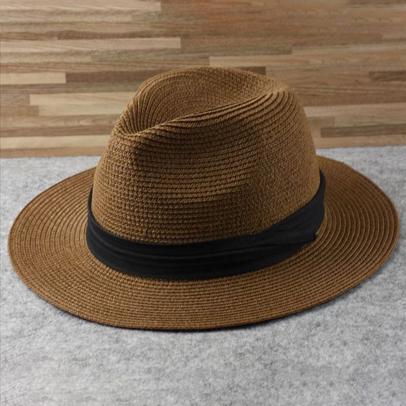 Chapeau Fedora en paille marron avec bande noire, posé sur une surface grise, fond en bois. Accessoire mode élégant et tendance pour l'été.