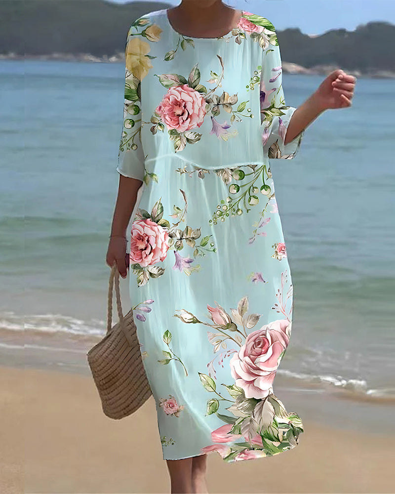 Robe longue fleurie femme, manches trois-quarts, fond bleu clair, motif floral rose, plage en arrière-plan, style estival élégant.