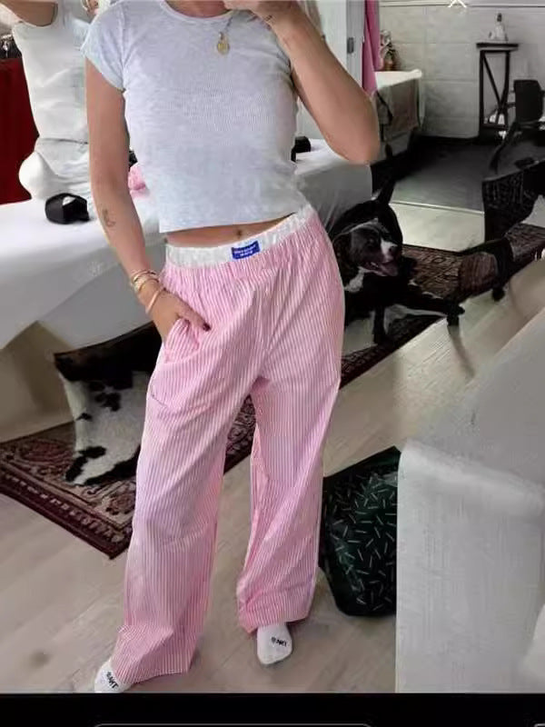 Femme portant un t-shirt blanc court et un pantalon rose à rayures, posant dans une chambre moderne. Mode décontractée, style tendance.