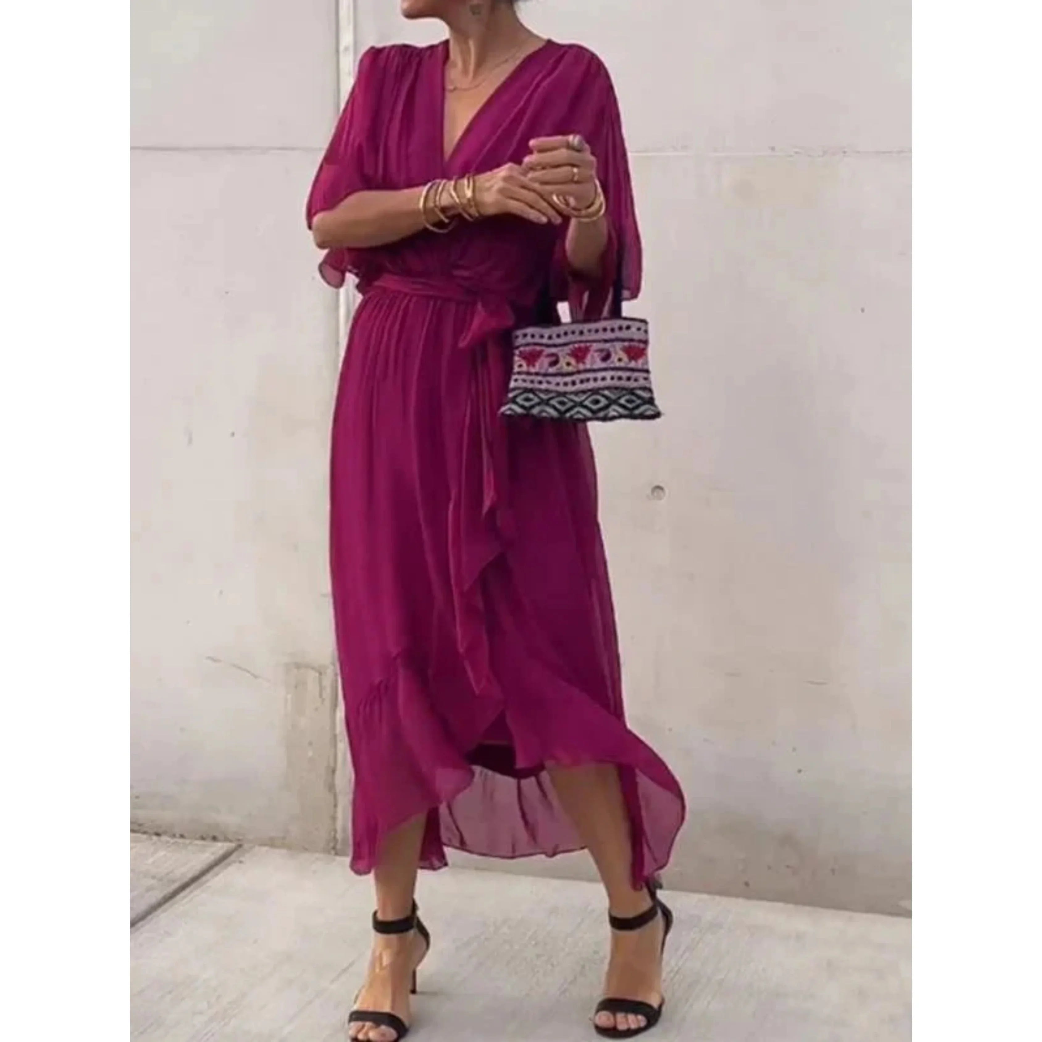 Robe longue fuchsia élégante, femme tenant un sac à motifs ethniques, sandales noires à talons, style chic et tendance, mode féminine moderne.