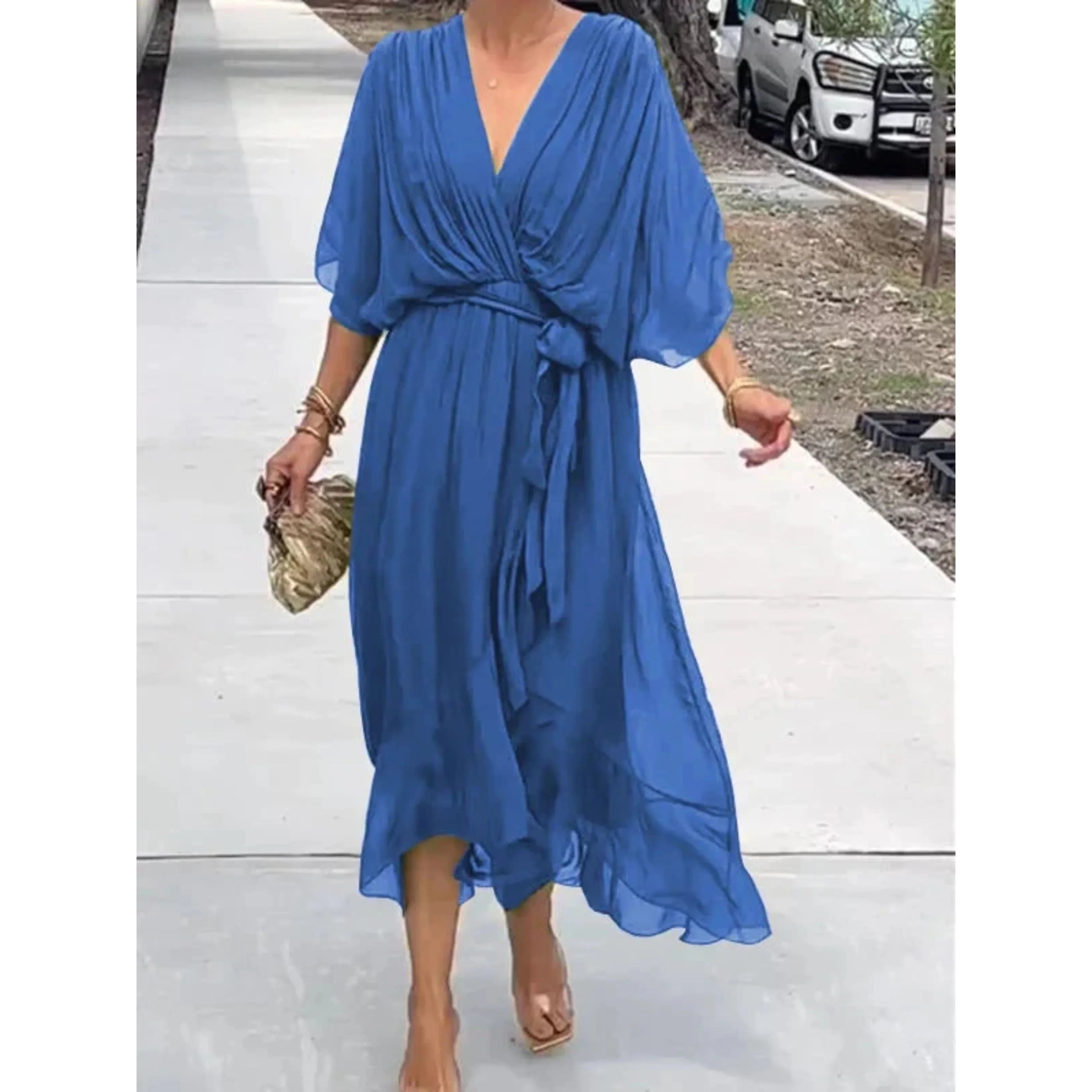 Robe bleue fluide élégante avec manches chauve-souris, ceinture nouée à la taille, portée par une femme marchant sur un trottoir. Mode féminine chic.