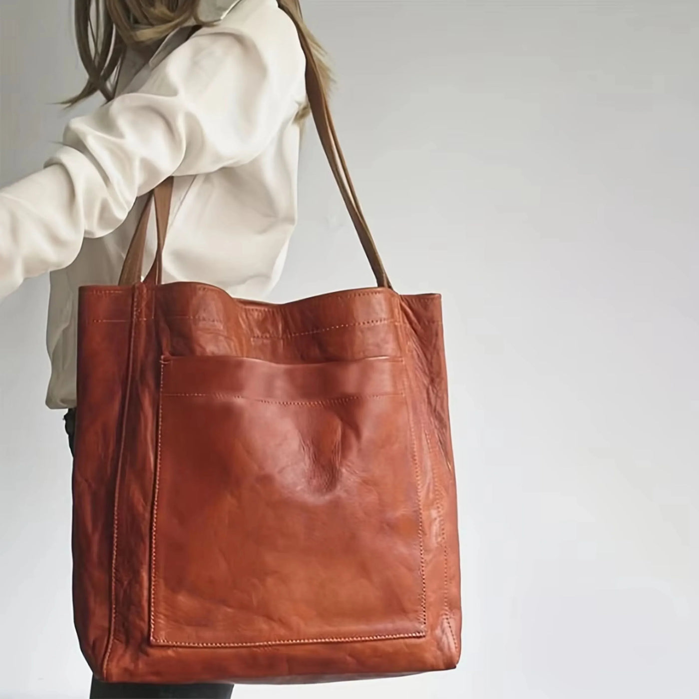 Sac en cuir marron porté par une femme en chemise blanche, design élégant et spacieux, idéal pour le shopping ou le bureau. Accessoire mode tendance.