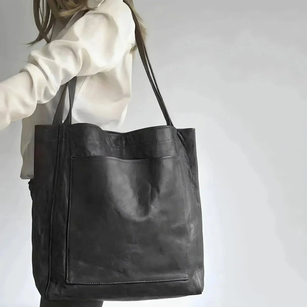 Sac cabas en cuir noir porté par une femme, design minimaliste, grande poche avant, idéal pour mode urbaine et élégante. Accessoire tendance.