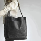 Sac cabas en cuir noir porté par une femme, design minimaliste, grande poche avant, idéal pour mode urbaine et élégante. Accessoire tendance.