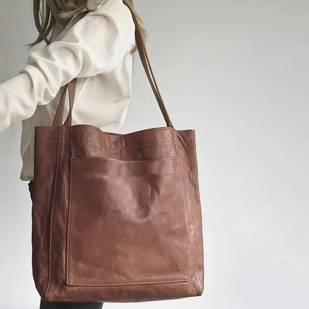 Sac en cuir marron porté par une femme en chemise blanche, design minimaliste avec grande poche avant, accessoire mode élégant et pratique.