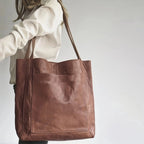Sac en cuir marron porté par une femme en chemise blanche, design minimaliste avec grande poche avant, accessoire mode élégant et pratique.