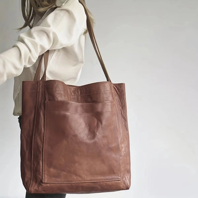 Sac en cuir marron porté par une femme en chemise blanche, design minimaliste avec grande poche avant, accessoire mode élégant et pratique.