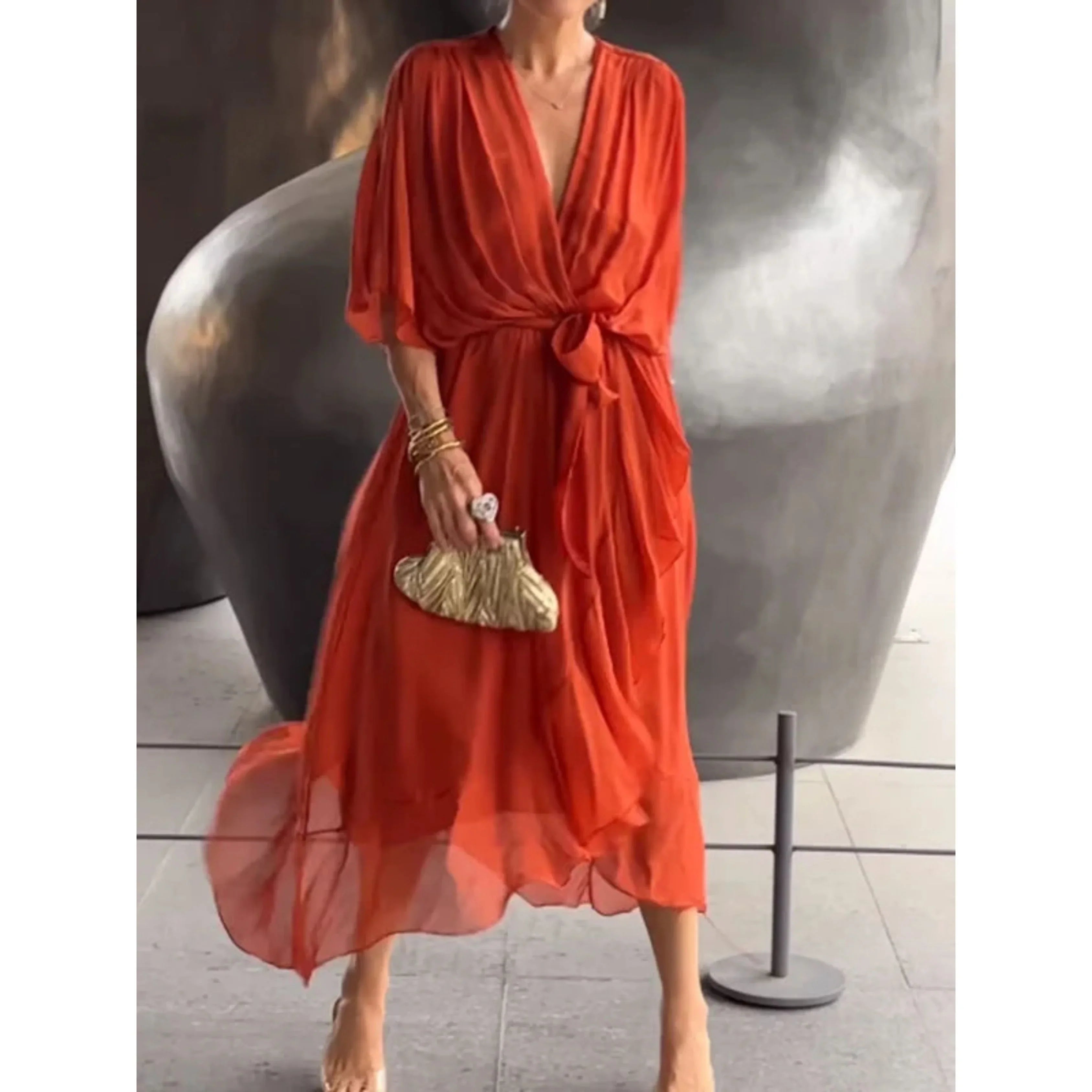 Robe rouge élégante en mousseline, ceinturée à la taille, portée par une femme tenant une pochette dorée. Mode féminine chic et tendance.